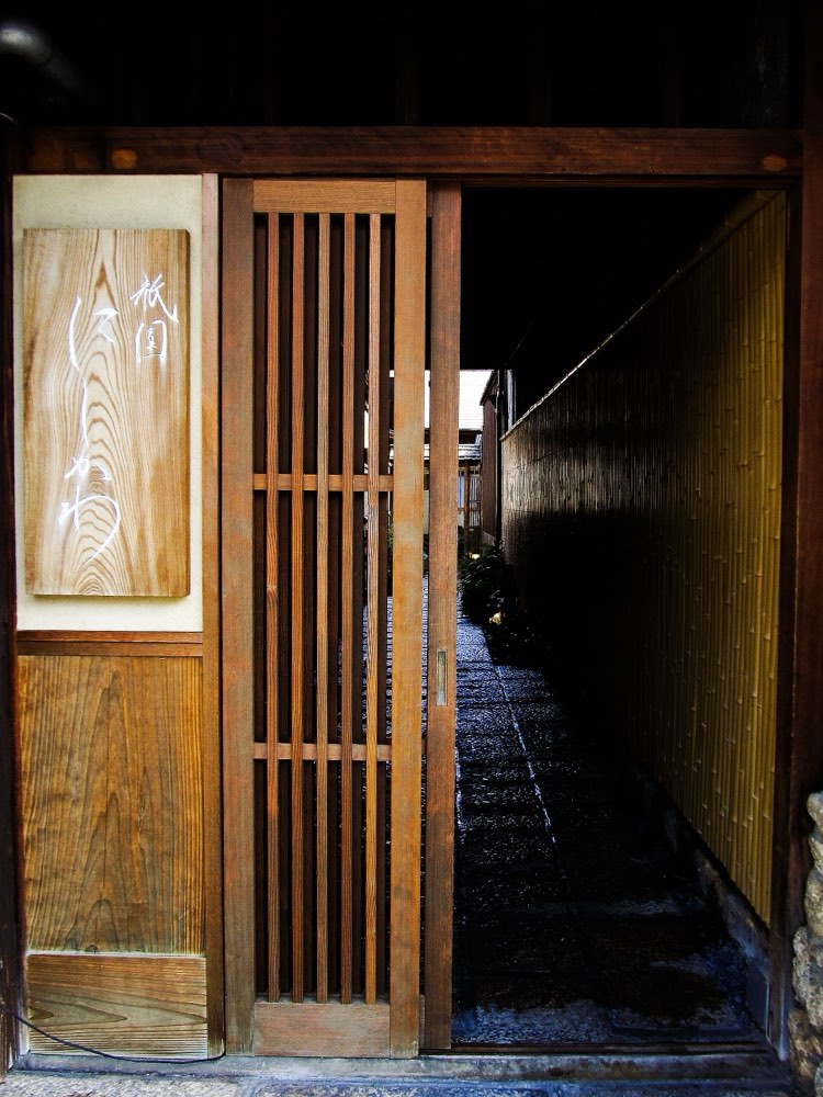 The wooden entrance and name board of Gion Nishikawa, opening onto a stone path, Kyoto